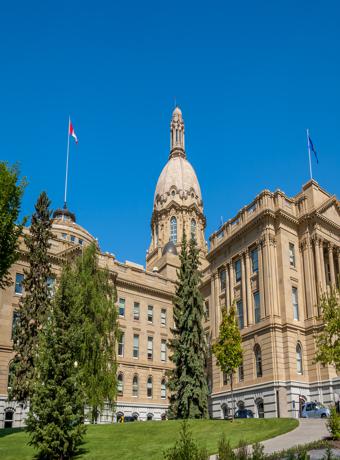 lberta Legislature Building in Edmonton under a clear blue sky, showcasing the elegant Beaux-Arts architecture surrounded by lush greenery.