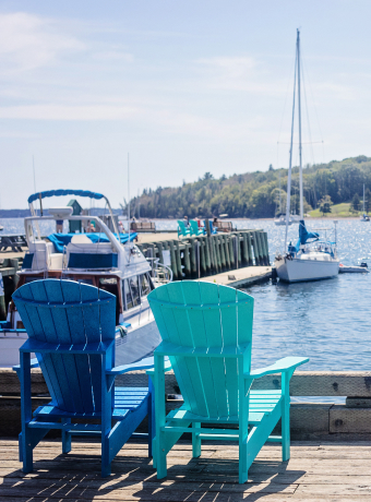 Two Adirondack chairs facing a serene marina with boats at a dock, embodying a peaceful Canadian lakeside moving destination.