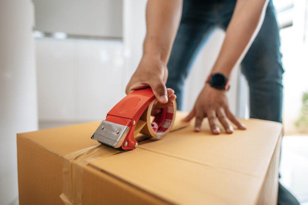 Close up hand of CPM moving team uses glue tape to close cardboard box, sealing big box for packing