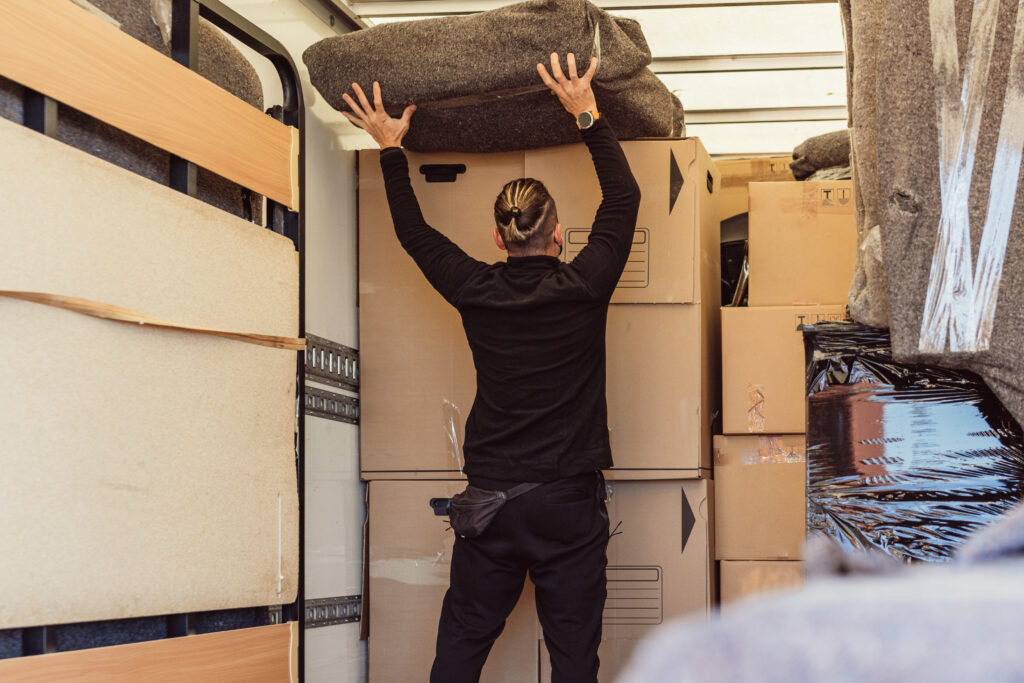 Professional Mover placing a bundle on top of cardboard boxes inside a moving truck.